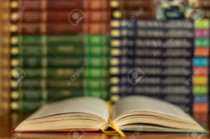 Education learning concept with opening book or textbook in old library, stack piles of literature text academic archive on reading desk and aisle of bookshelves in school study class room background